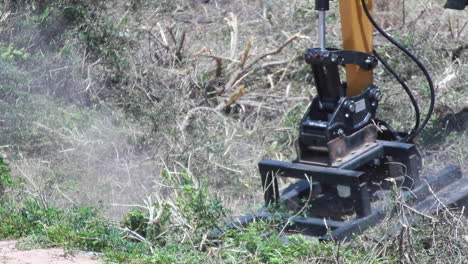 primer plano en cámara lenta de un brazo de maquinaria de planta amarilla y negra con una cadena, cortando y deshierbando algunos arbustos semisecos en españa