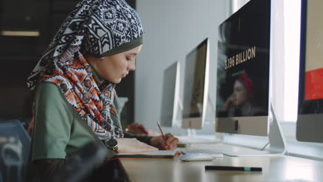 mujer de negocios en hijab usando computadora y tomando notas