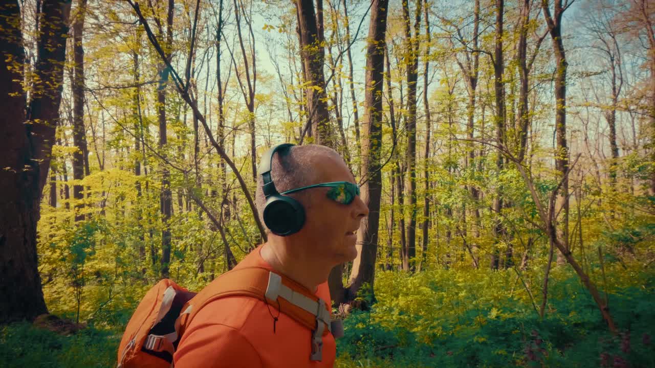 Ein moderner Mann mittleren Alters in den 50ern mit kabellosen Kopfhörern und Sonnenbrille beim Wandern. Schnittstelle von Technologie, Gadgets und aktivem Outdoor-Lebensstil. 4K-Qualität