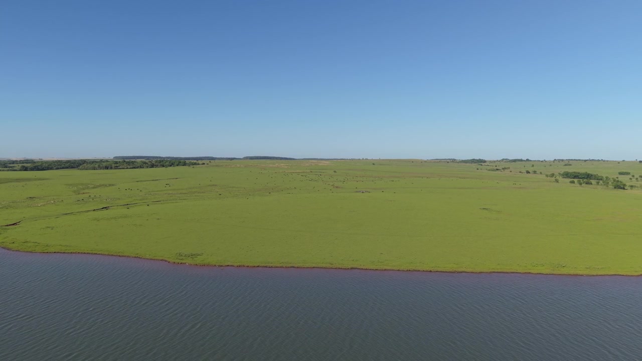 Droneoptagelse med zoom ind fra luften af en grøn mark med en sø.