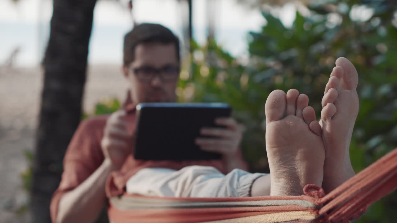 hombre relajándose en una hamaca en la playa con una tableta