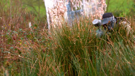 man crouching in the grass shooting paintball gun