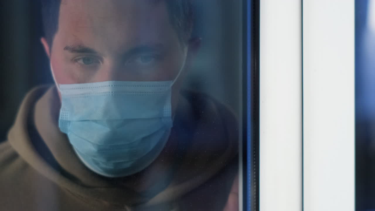 마스크를 착용 한 남자가 창문을 통해보고 있습니다.