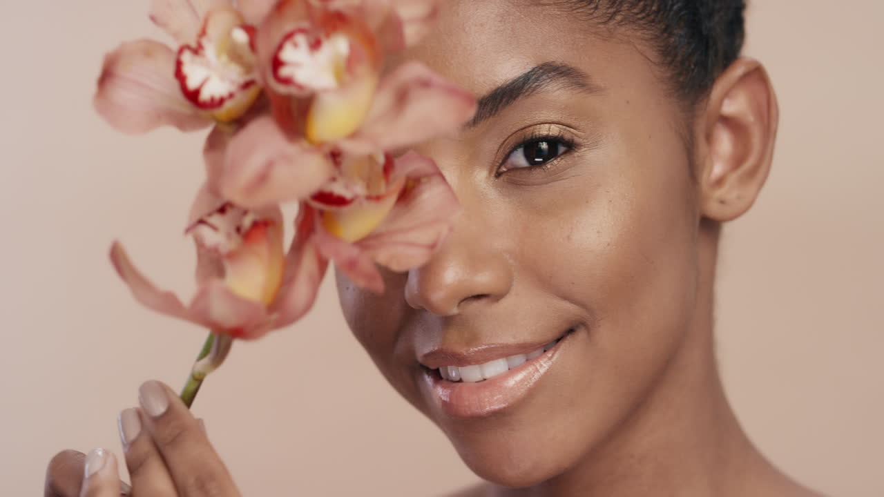 ritratto di bellezza bella donna afroamericana che posa giocosamente con un fiore di orchidea toccando una pelle sana che gode di una dolce fragranza di essenza naturale concetto di cura della pelle