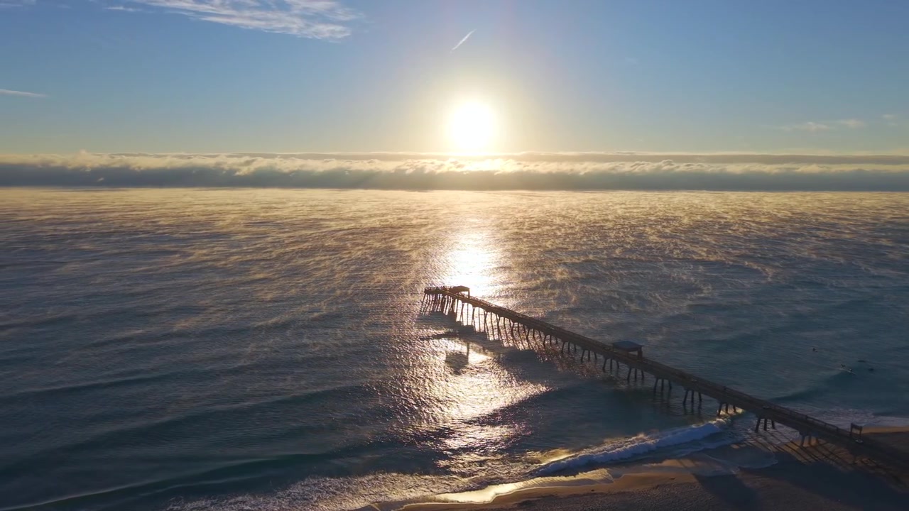 Rotating aerial drone shot above Deerfield Beach at sunrise on a cold morning with steam rising off the ocean and stunning golden light