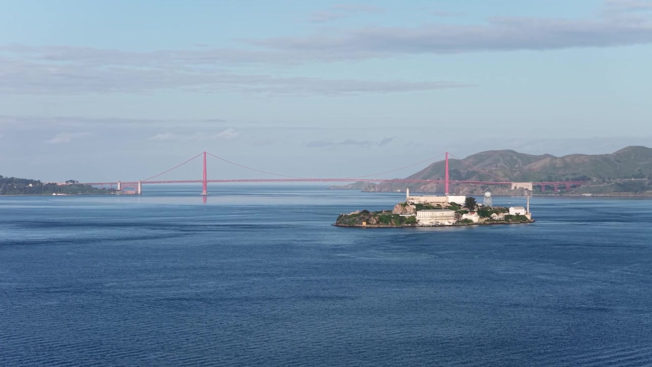Kaliforniya, Amerika Birleşik Devletleri'nde sakin ve güneşli bir sabah, açık gökyüzü altında sakin mavi suların üzerinde, arka planda Golden Gate Köprüsü ile San Francisco Körfezi'ndeki Alcatraz Adası. Havadan panorama.
