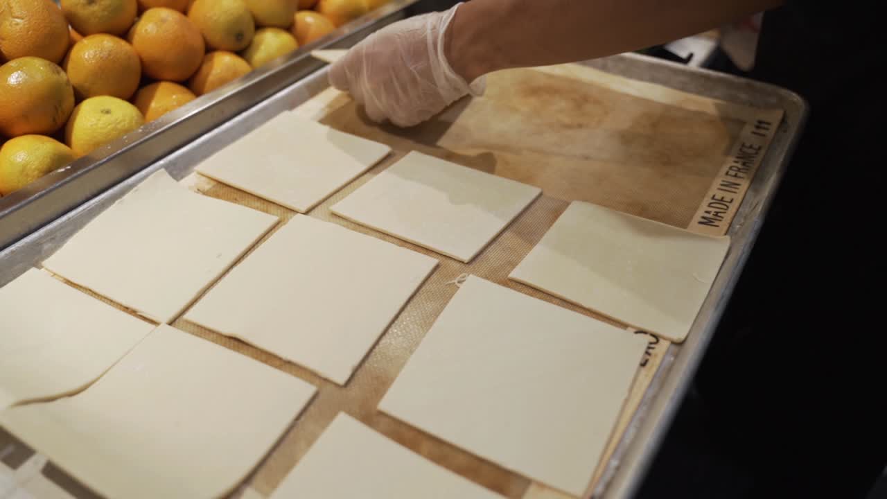 The pastry chef is placing small sheets of puff pastry on a baking tray.