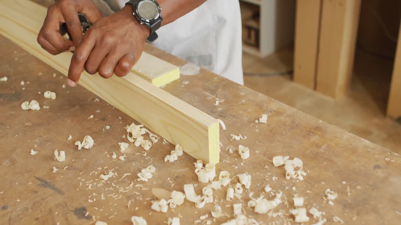Close up of male carpenter's hands planing a plank of wood with a hand plane in a carpentry shop