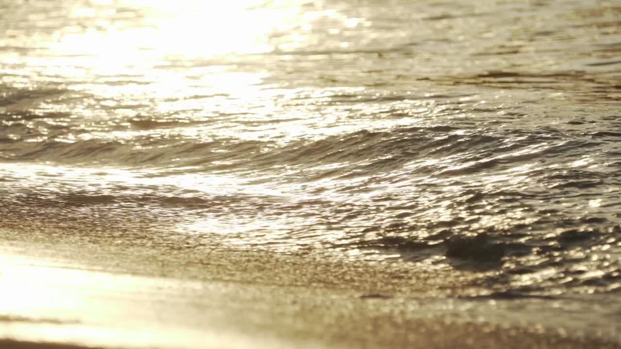 모래 해변의 해안에 있는 작은 파도의 느린 동작 샷, 수면에 밝은 햇빛 반사