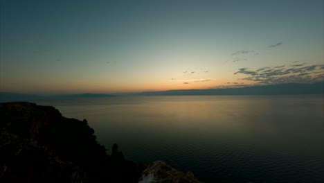 Timelapse-De-Un-Amanecer-En-Lin-Albania-Por-La-Mañana-Vigilando-El-Agua-Con-Las-Montañas-De-Macedonia-Al-Fondo-En-Un-Día-Claro-Con-Un-Cielo-Naranja