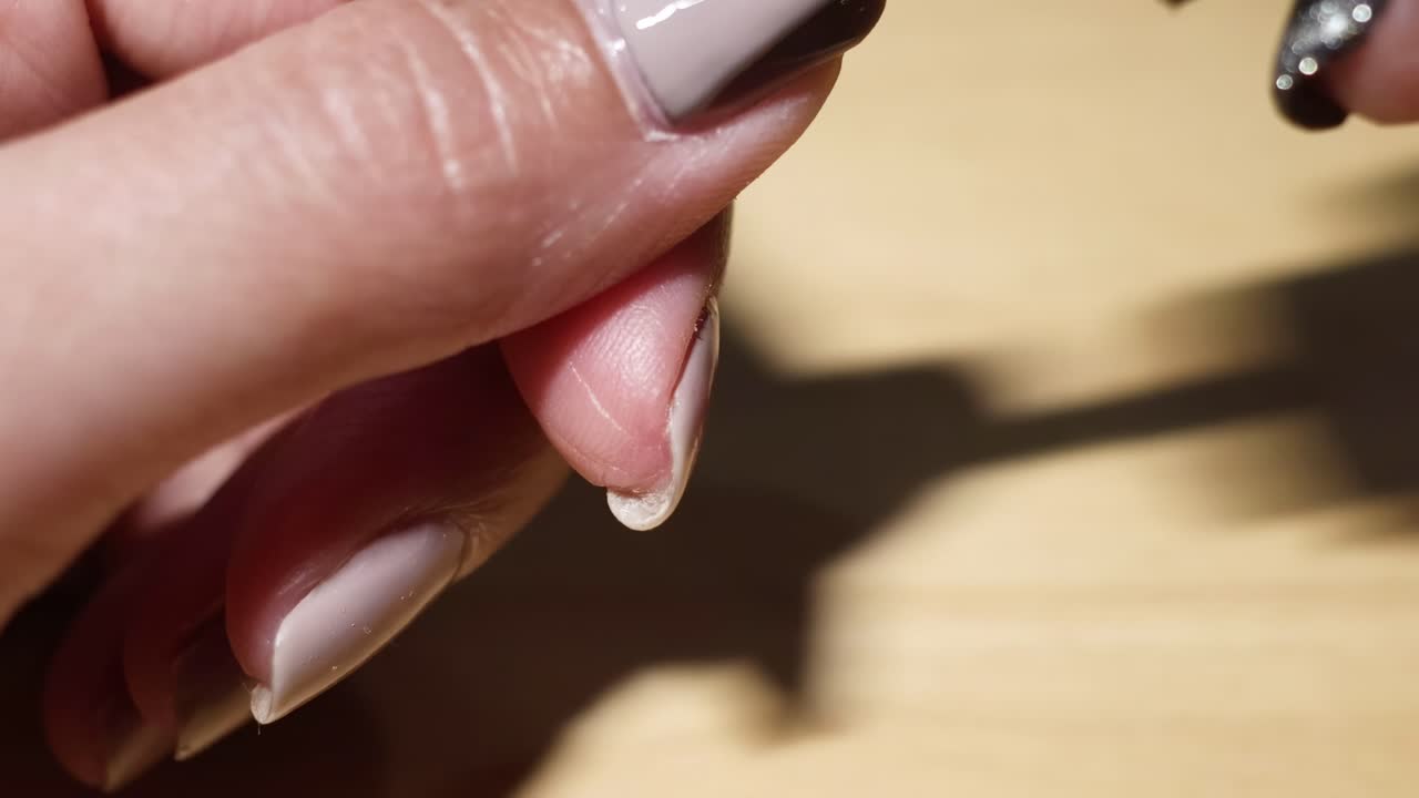 Detailed view of taupe nail polish being applied to fingernails on a wooden surface.