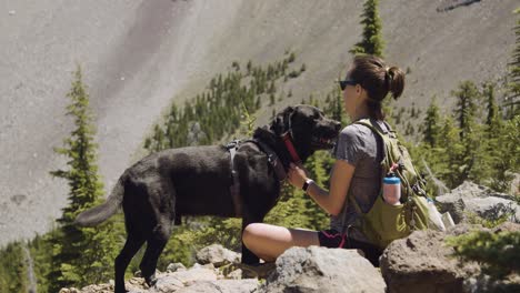 chica y laboratorio negro tomando un descanso en una caminata con la montaña en el fondo