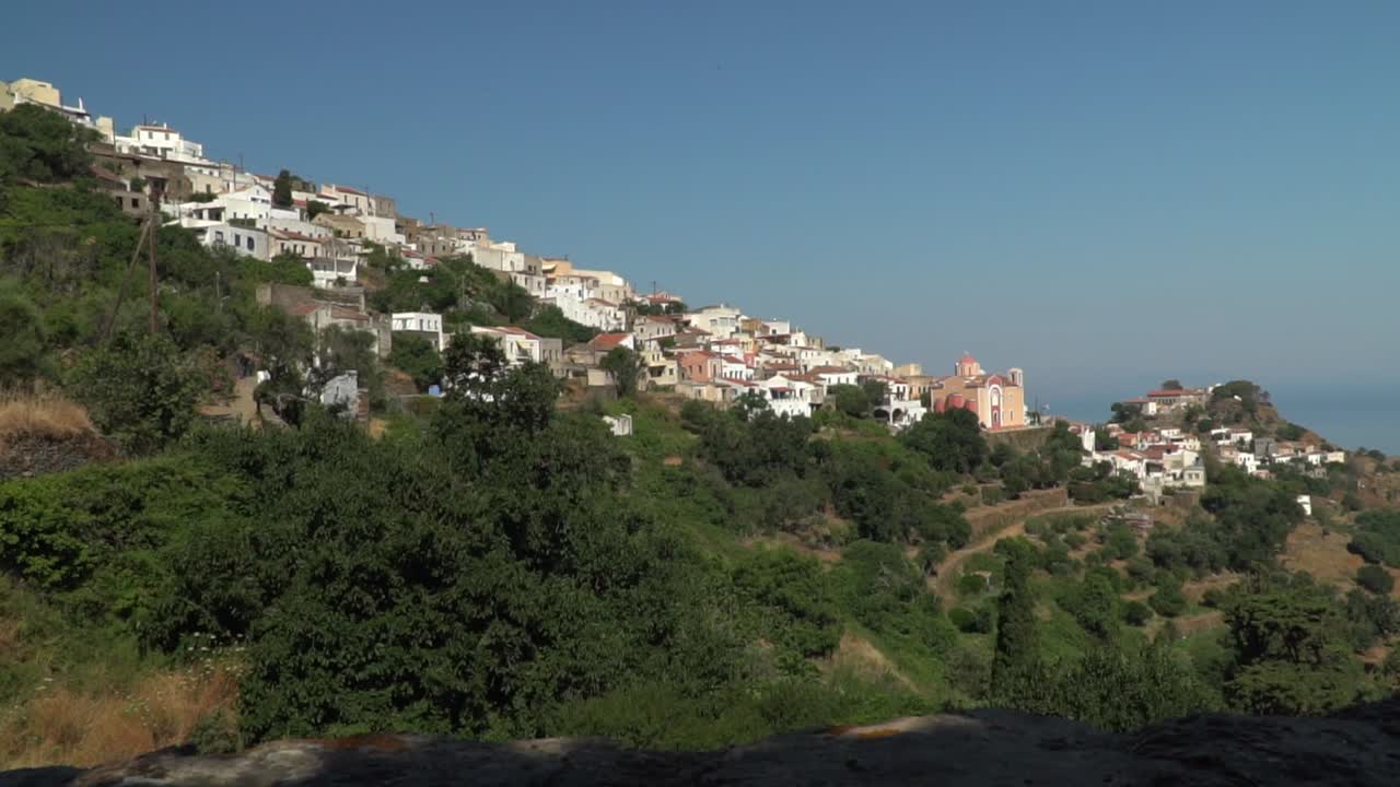 Right pan from back of girl with summer hat, looking out on Greek town on hill in distance