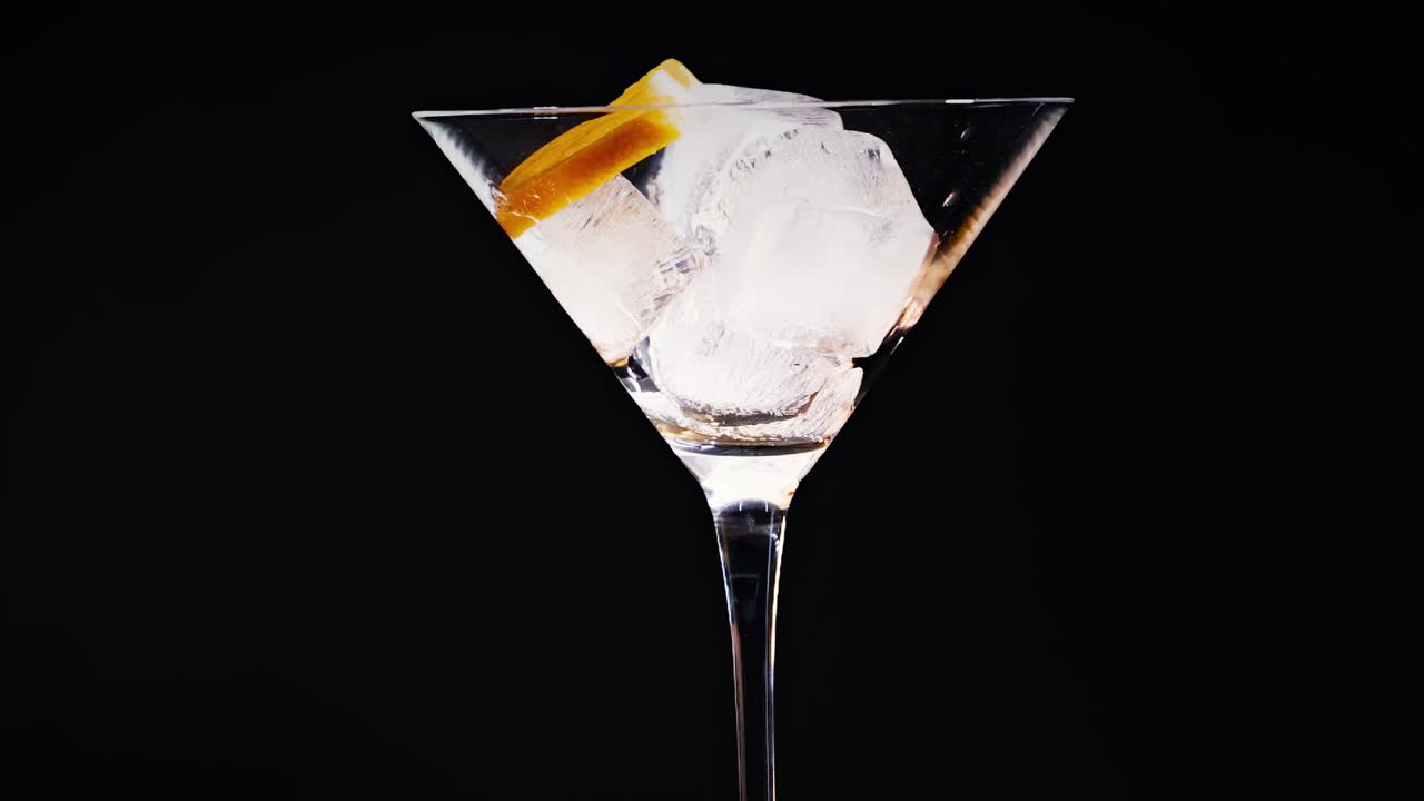 A series of martini glasses with ice cubes and orange garnish against a black background.