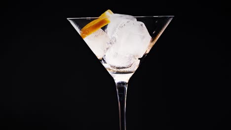 a series of martini glasses with ice cubes and orange garnish against a black background.