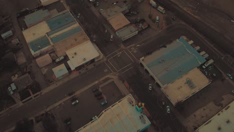 Top-down-cinematic-city-aerial-view-of-downtown-Roseville,-California-with-industrial-buildings,-shops-and-cars-driving-by-during-sunset-golden-hour