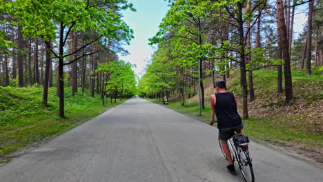 Hombre-Montando-Bicicleta-Por-El-Parque-Entre-árboles-Altos---Toma-De-Seguimiento