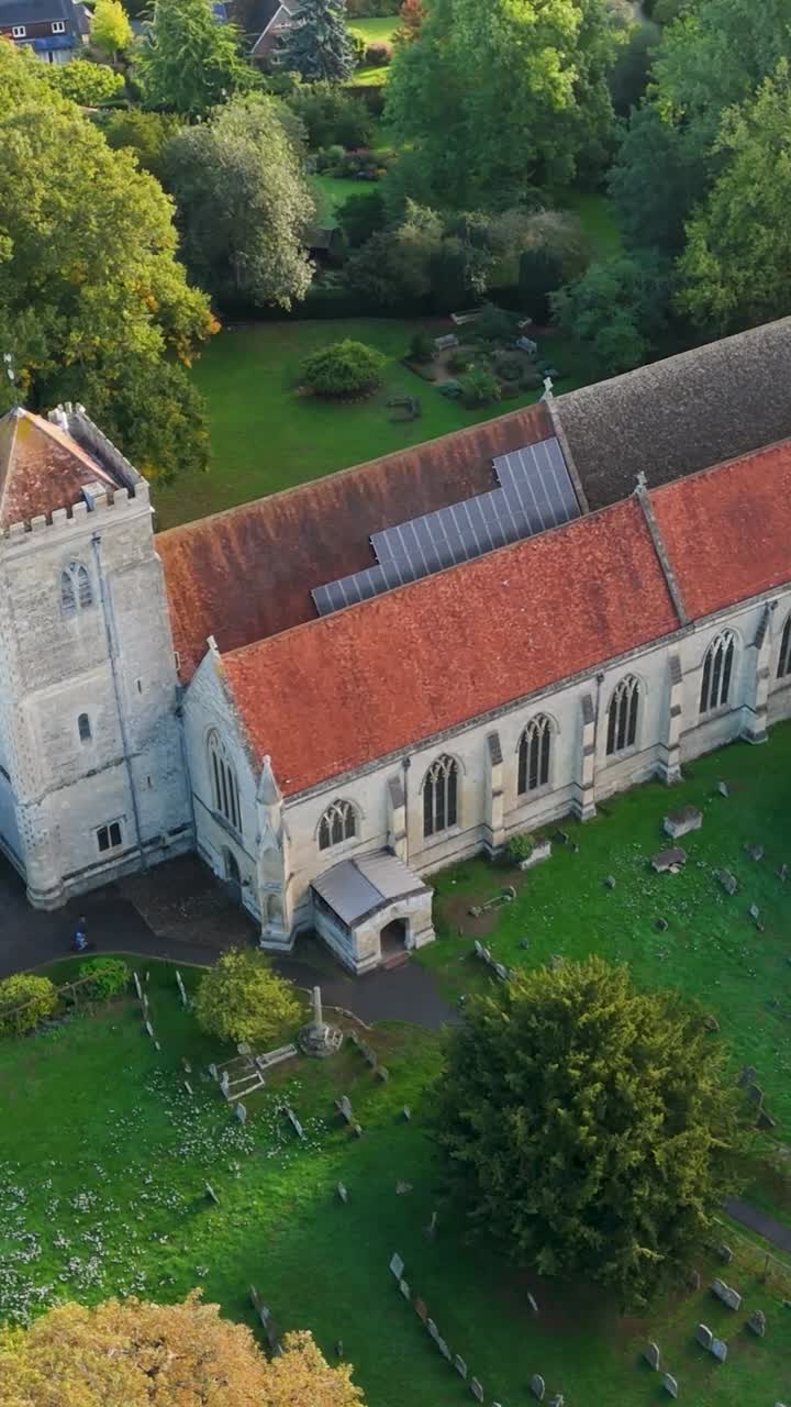 Vertical aerial drone orbit of Dorchester Abbey in Oxfordshire, England. Shot in morning light, the drone circles clockwise from the abbey frontage, showing the graveyard and village landscape