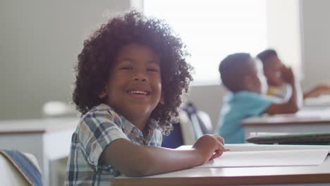 Video-of-happy-african-american-boy-sitting-at-desk-during-lesson-in-classroom