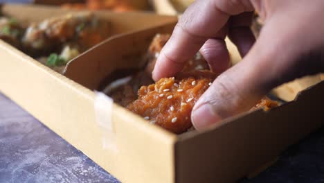 mano alcanzando el pollo frito coreano en una caja de cartón