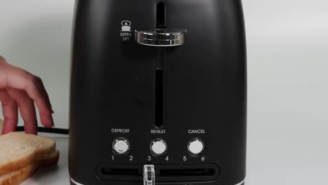 a hand adjusts the settings on a black toaster with bread nearby.