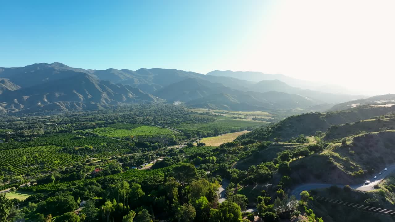 Sliding Aerial Shot Of Cars Driving Down A Mountain Into A Valley Of Farm Land In Ojai, California