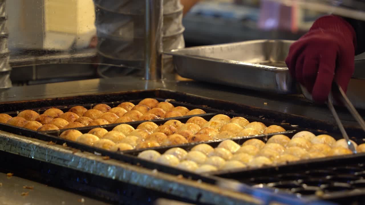 cocina japonesa bolas de takoyaki primer plano, chef profesional haciendo la comida callejera crujiente en una sartén moldeada caliente en el concurrido mercado nocturno en taiwán, asia