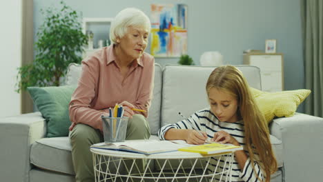 gray haired senior woman doing school homework together with her teen granddaughter and explaining her something