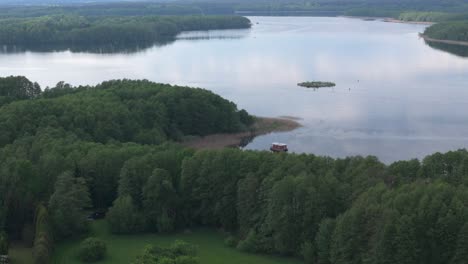 A-serene-aerial-view-of-a-beautiful-lake-house-nestled-in-a-lush-green-forest,-creating-a-tranquil-and-idyllic-scene