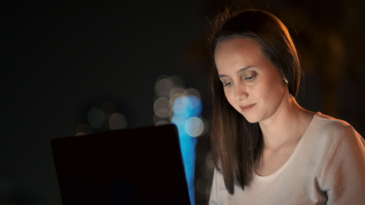 una mujer desarrolladora de software se sienta en un parque en una noche de verano en la ciudad y escribe código mirando la pantalla de una computadora portátil. imprime el artículo en una computadora portable. blogger responde a las publicaciones