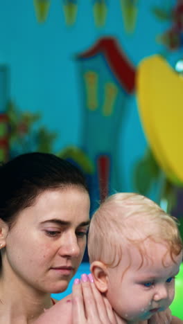 healthy gymnastics in the water for baby boy. female coach deeps the kid into the swimming pool. vertical video