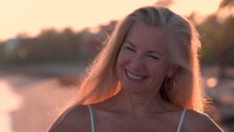 Portrait-of-beautiful-backlit-mature-woman-flipping-her-hair-across-her-head-while-on-a-tropical-beach-looking-at-camera-and-smiling