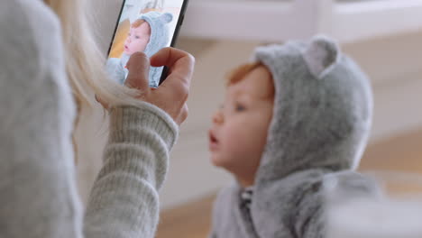 mother taking photo of baby using smartphone enjoying photographing cute toddler sharing motherhood lifestyle on social media