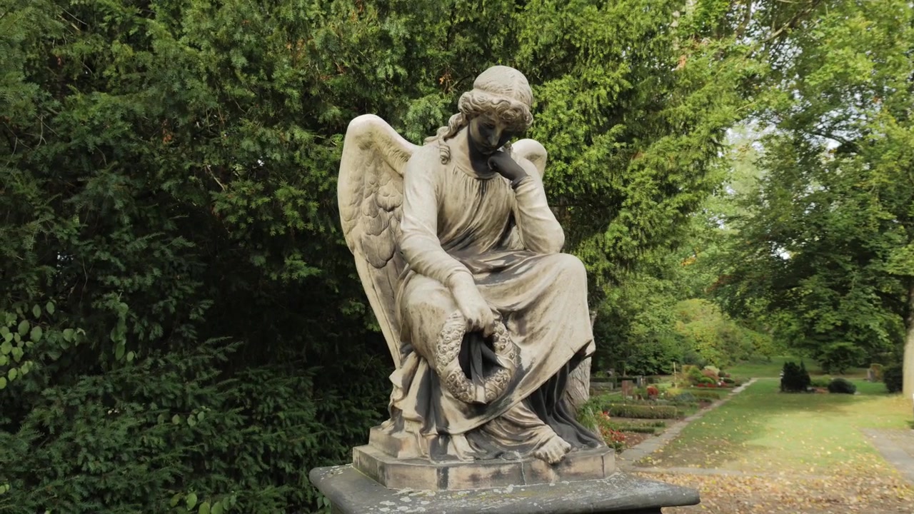 Statua di angelo femminile su un piedistallo in un cimitero con tombe sullo sfondo. Inquadratura ravvicinata con effetto parallasse