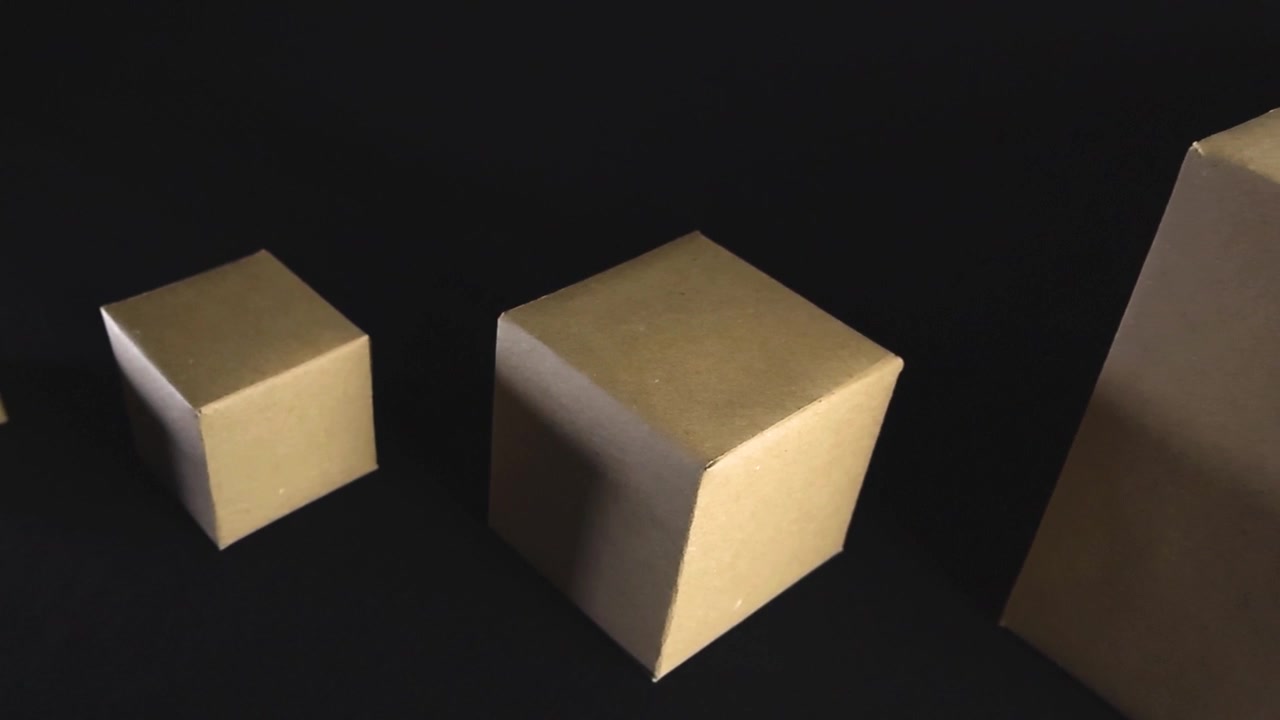Smooth gliding shot moving past several brown cardboard boxes of different sizes arranged in a row on a plain black background, representing concepts like logistics, shipping, and packaging