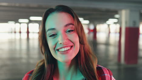 vista de cerca de una alegre joven caucásica sonriendo y mirando la cámara en un estacionamiento vacío