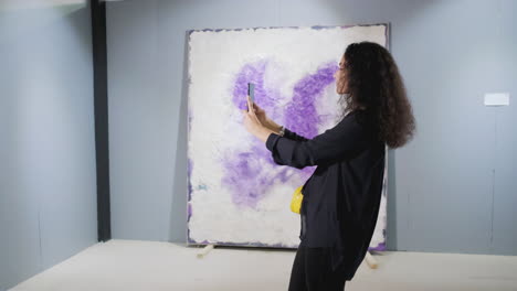 mujer tomando una foto de una pintura abstracta en una galería de arte