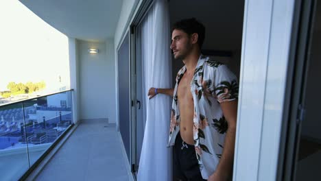 handsome young man walks from his hotel room to the balcony