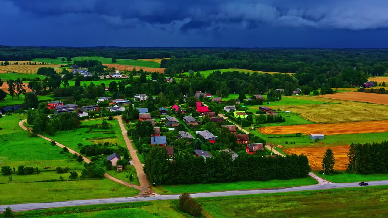 Colorful rural village surrounded by farmland under a moody stormy sky with lightning