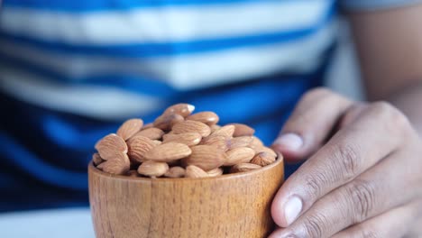 person eating almonds from a wooden bowl