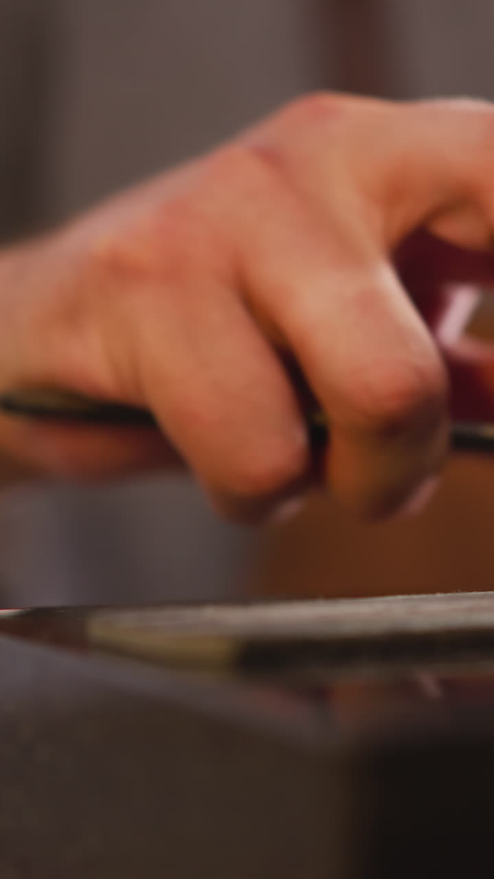 Male hand sharpens special cutter with sandpaper in craft workshop close view. Leathersmith prepares tool at workplace. Leather cutting instrument