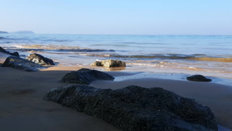 handheld low angle shot of small waves over rocks on beautiful deserted tropical beach
