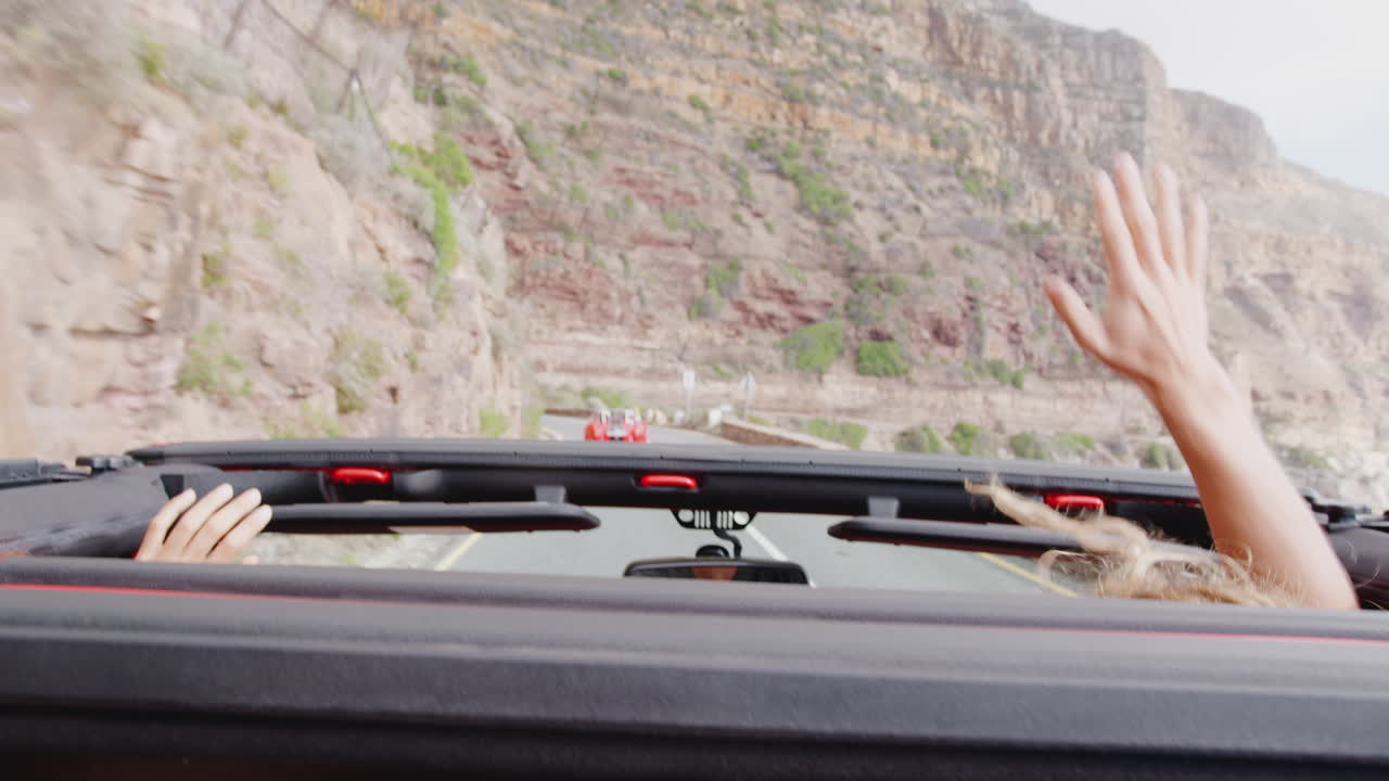 커플이 여름 휴가 동안 오픈  렌터 카의 지붕을 통해 흔들고 있습니다.