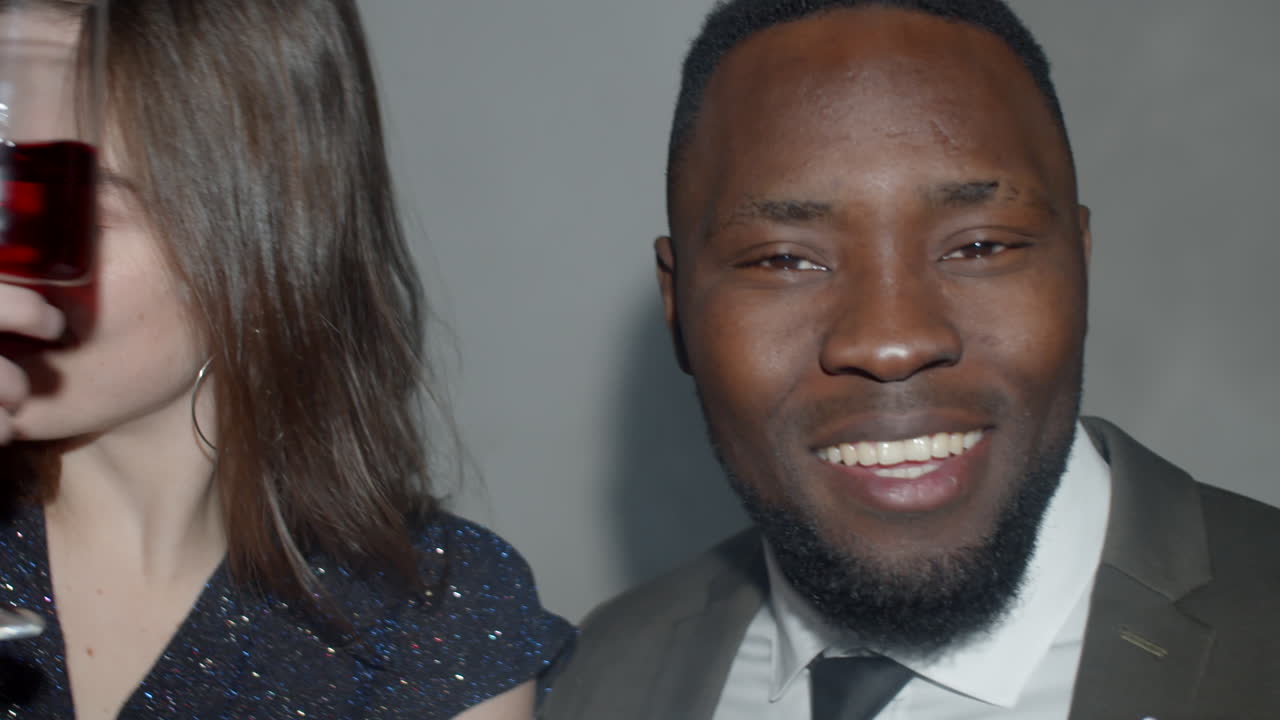 hermosa pareja multiétnica bailando con vino y sonriendo a la cámara
