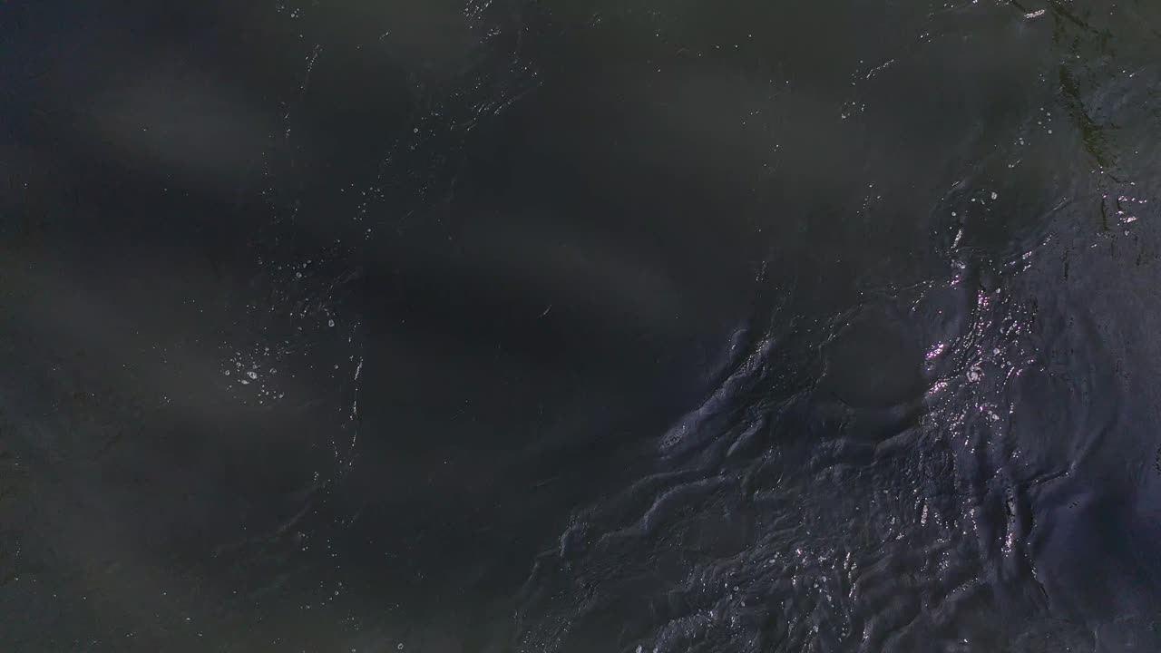 Close up perspective of deep dark river water rushing down steam.