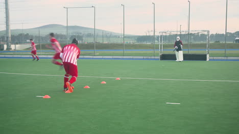playing field hockey, men practicing drills and shooting at goal on field
