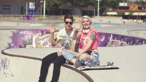 happy trendy young couple waving at the camera