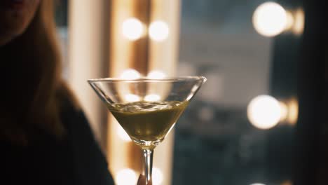 Hair-stylist-shows-of-mixed-hair-dye-in-martini-glass-swirling-thick-liquid-in-front-of-mirror-and-lights