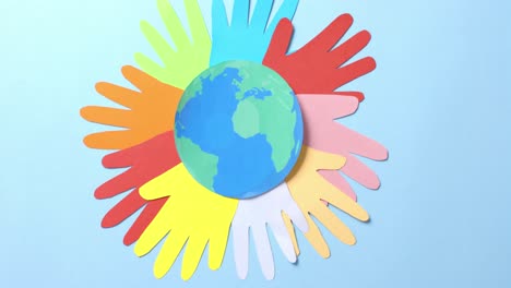 close up of hands together with globe made of colourful paper on blue background with copy space