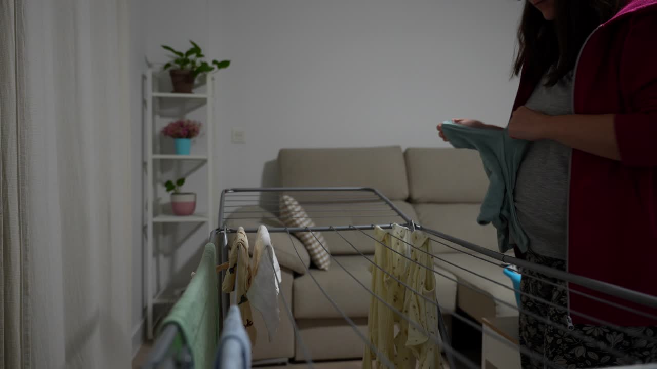 Close up of clothesline as woman hangs baby clothes in living room at night
